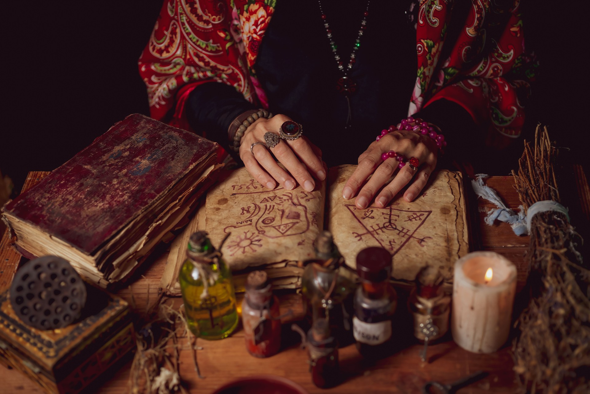 Female witch making potion on dark background, magic bottles with potions and candles on table of alchemist, Halloween theme